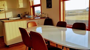 Ein Essbereich mit einem weißen Tisch und vier Stühlen, eine Küche mit Holzschränken und einem Fenster, sowie Blick auf eine flache Landschaft.