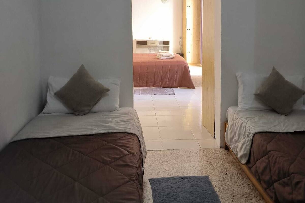 Une chambre avec deux lits, une armoire en bois et une salle de bain visible à travers une porte ouverte.