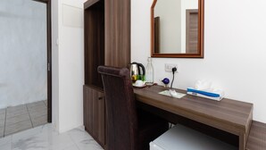 A room with a wooden desk, a mirror, a chair, and a small cabinet.