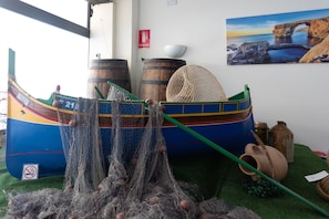 Un modelo de barco con redes de pesca, barriles y un cubo verde sobre una superficie verde.