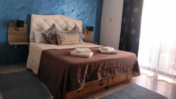 A bedroom with a blue wall, a tufted headboard, two bedside tables with lamps, a bed with a brown bedspread, and a window with sheer curtains.