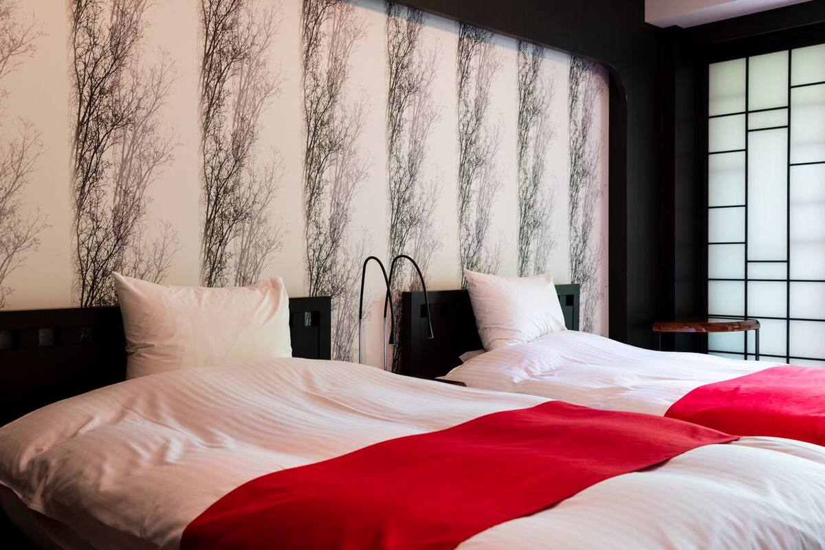 A hotel room with a large bed, a headboard with a tree design, and a window with blinds.