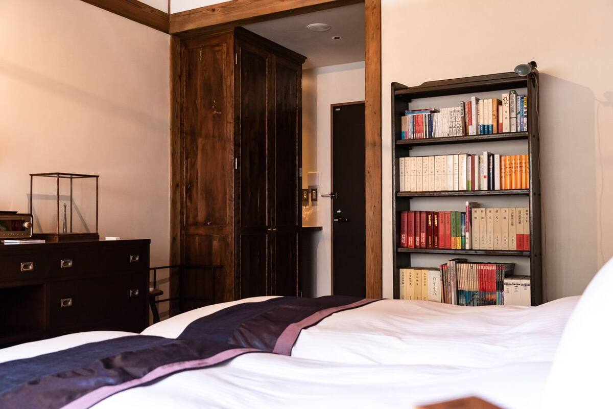 A bedroom with a bed, a wooden wardrobe, and a bookshelf filled with books.