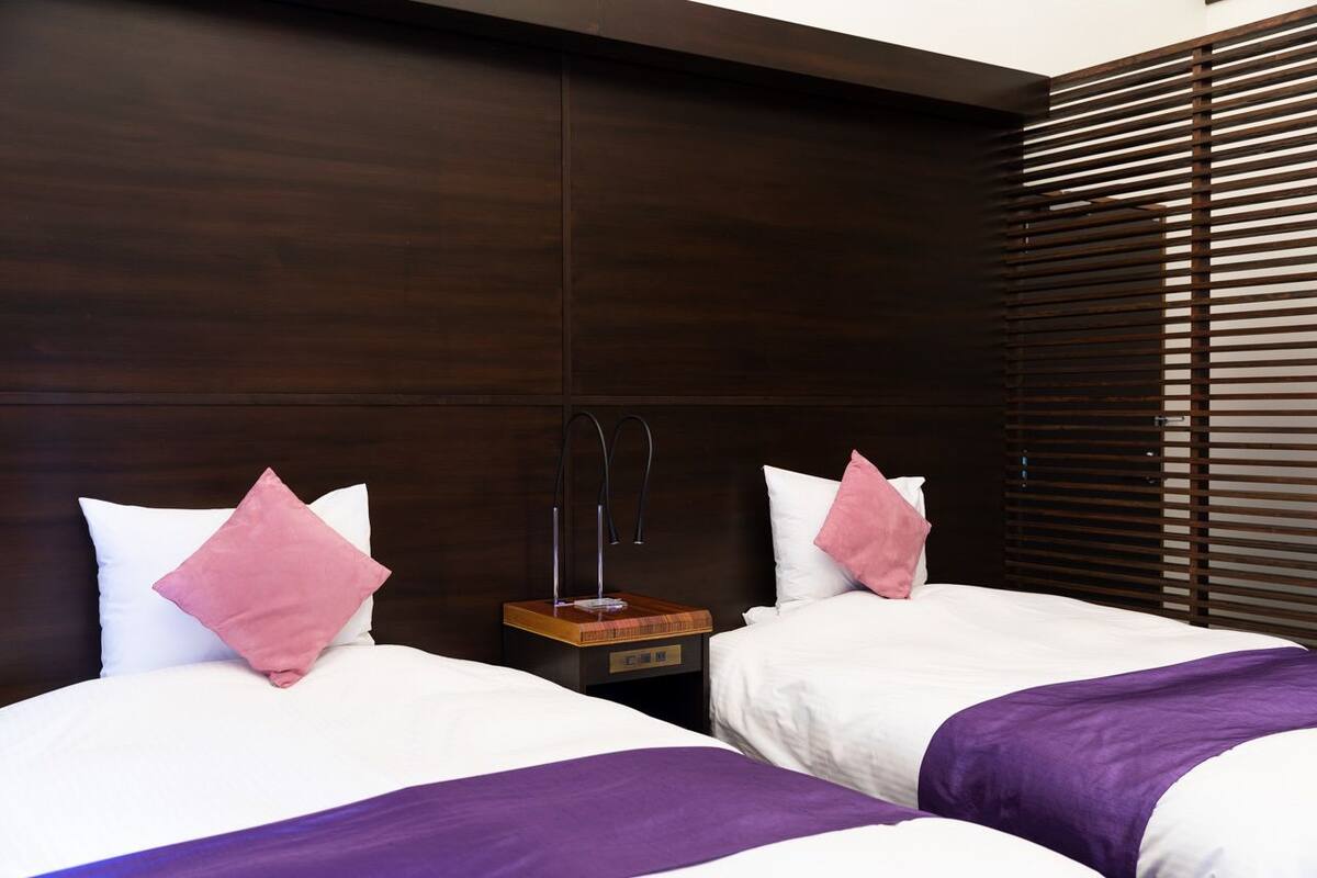 A hotel room with two beds, wooden headboard, and a nightstand with a lamp.