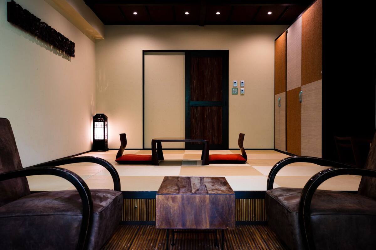 A room with a wooden bench, two chairs, a small table, a lantern, and a sliding door.