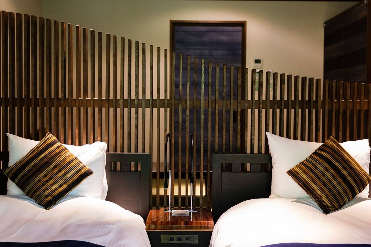 A hotel room with two beds, each with a pillow and a bedside table.