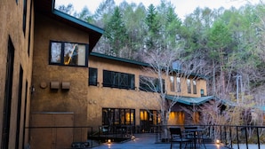 A building with a wooden deck, outdoor seating, and a view of trees. - Ancient Hotel asama karuizawa (Karuizawa)
