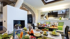 A modern kitchen with a dining area, featuring a brick archway, a flat-screen TV, and a variety of breakfast items on the table. - Al Dolce Farniente (Marsciano)