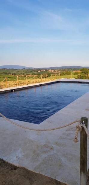A rectangular pool with a rope barrier, surrounded by a paved area and a view of distant hills. - Al Dolce Farniente (Marsciano)