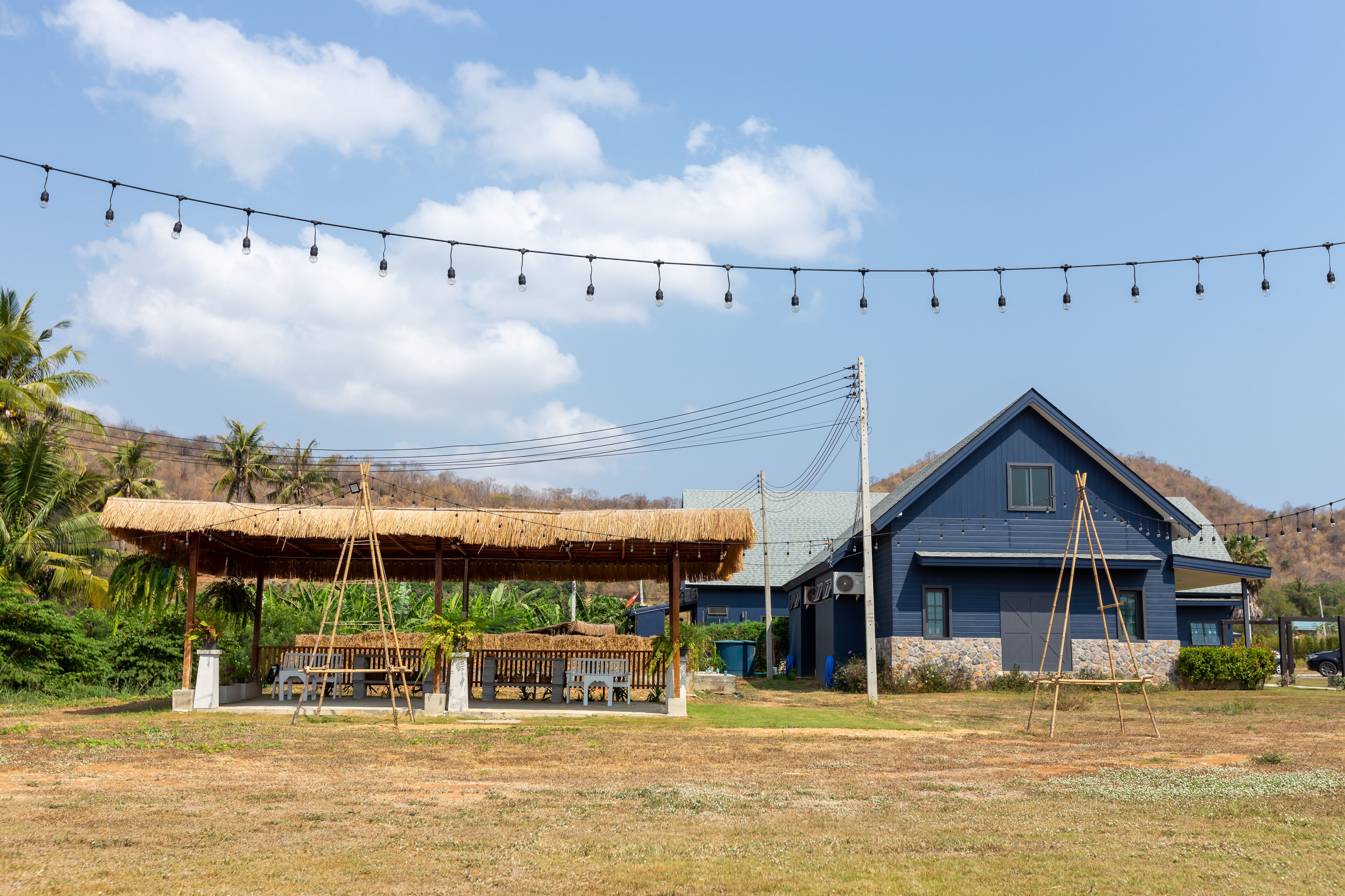 A house with a blue exterior, a thatched-roof structure, and a swing set in the yard.