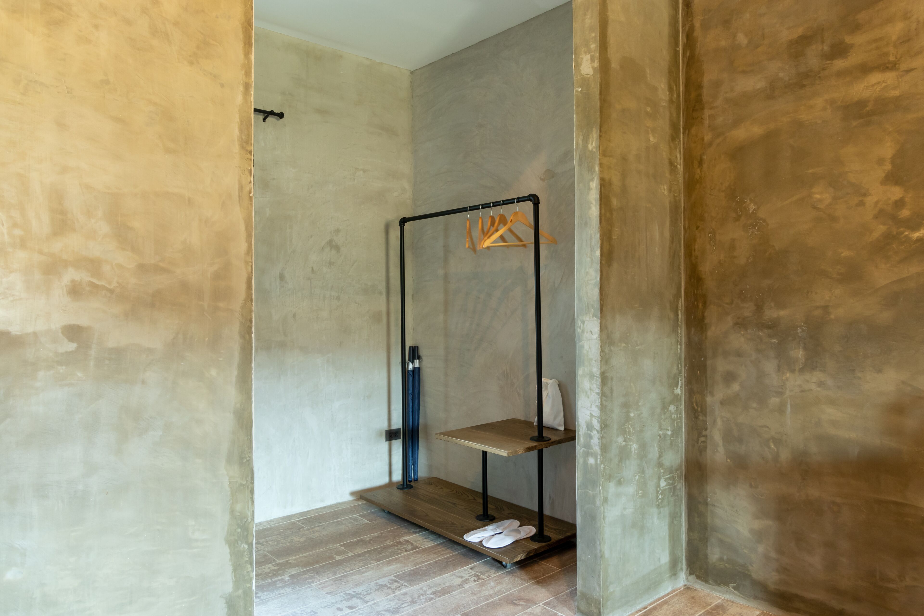 A minimalist bathroom with a concrete wall, a wooden shelf, and a black metal rack.