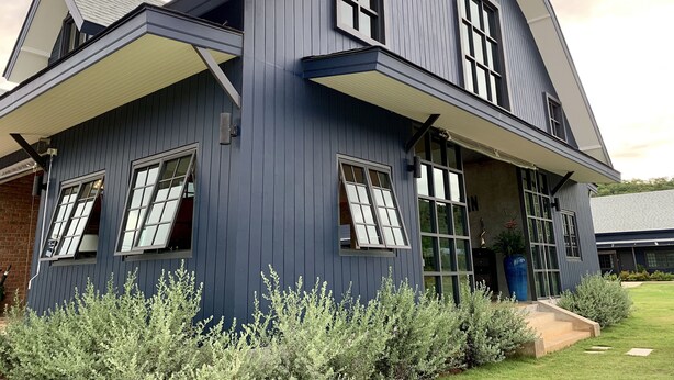 Et moderne hus med to etager, mørkeblå facade, store vinduer og en velplejet græsplæne.