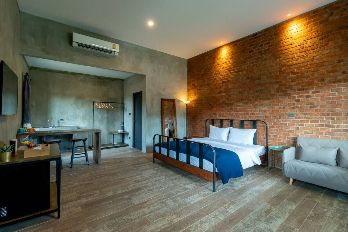 Quarto moderno com parede de tijolos, uma cama, uma escrivaninha e um sofá.