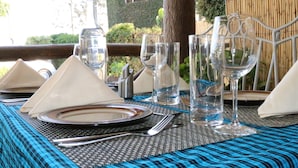 A table set for dining with clear glassware, plates, and cutlery, set against a bamboo backdrop and a wooden railing. - Dan Stam Hotel (Arusha)