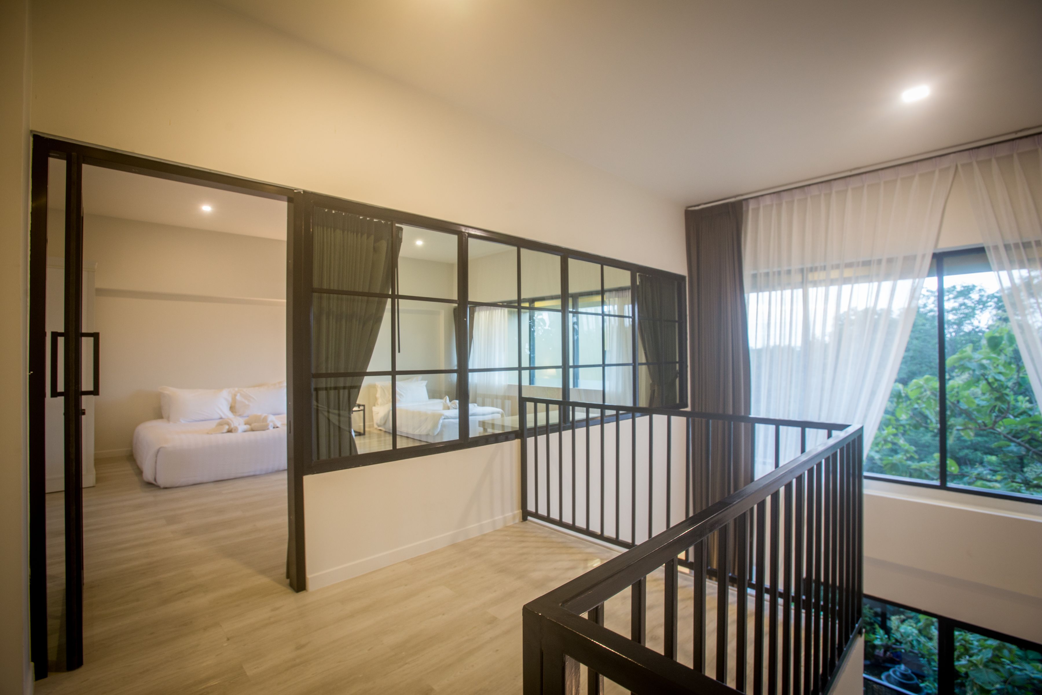 Un interno moderno con una scala, una camera da letto con un letto e tende, e vista sul verde circostante.