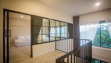Un interno moderno con una scala, una camera da letto con un letto e tende, e vista sul verde circostante.