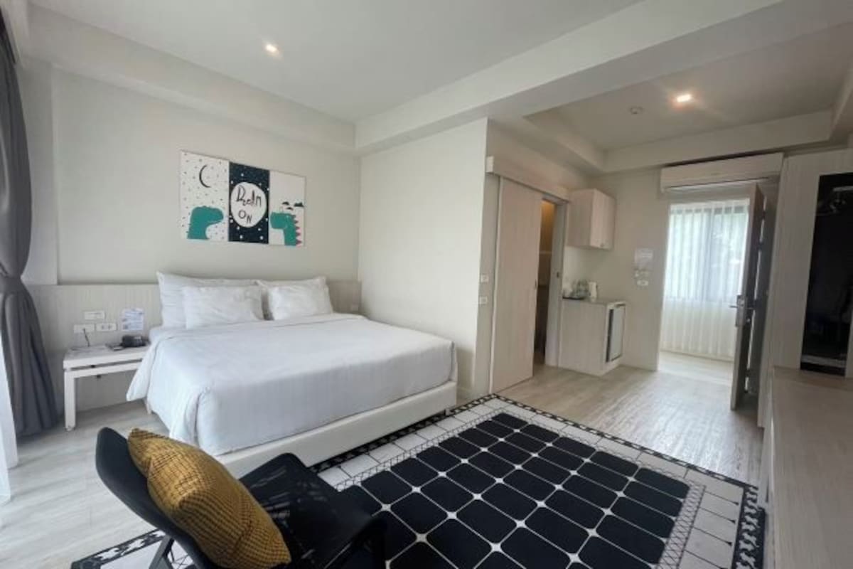 Un dormitorio con cama, mesita de noche, silla, alfombra con estampado blanco y negro y una pared con arte abstracto.