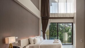 Una habitación de hotel moderna con una cama grande, un escritorio y vistas a zonas verdes por las ventanas.