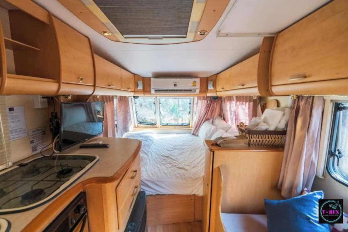 Interior compacto de una caravana con kitchenette, cama y una pequeña zona de estar.