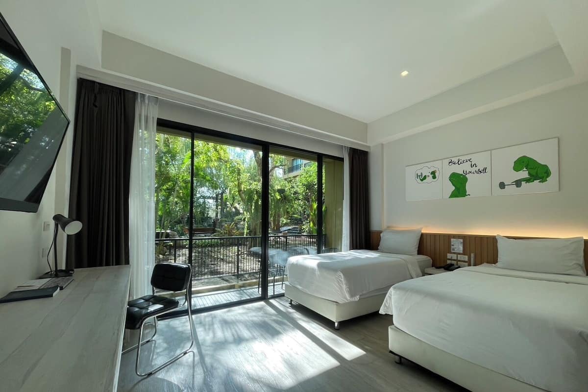 Habitación de hotel moderna con dos camas, un escritorio, una silla, un televisor y un balcón con vistas a zonas verdes.