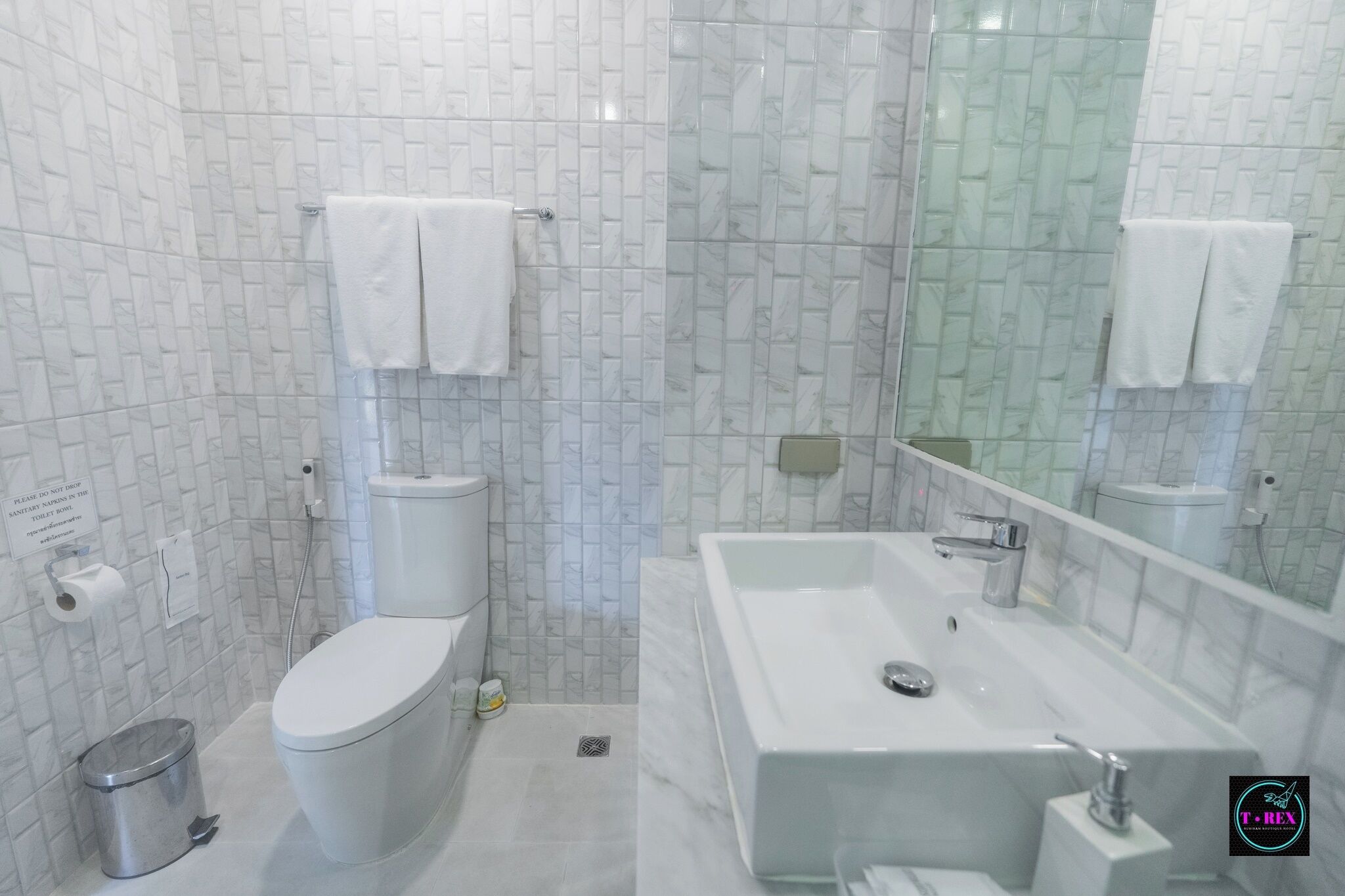 Un baño con inodoro, lavamanos y espejo. Hay toallas colgadas en la pared.
