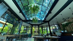 Un restaurante con techo de vidrio que permite vistas de la vegetación circundante. Mesas y sillas dispuestas para comer.