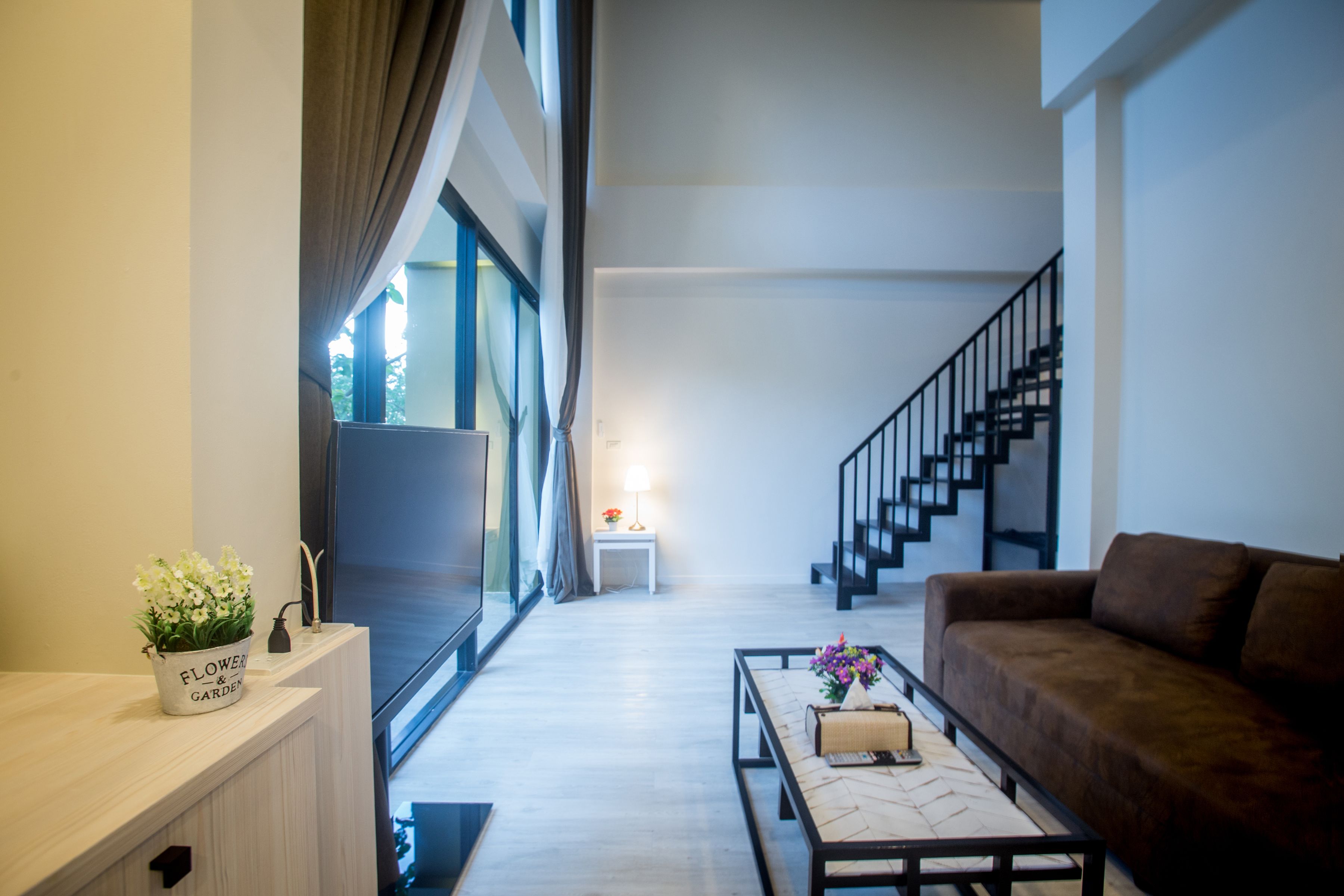 A modern living room with a sofa, coffee table, and a potted plant. A staircase is visible in the background leading to another level.