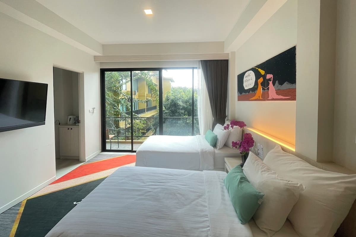 Habitación de hotel con dos camas, un televisor, un cuadro y vistas a un edificio y áreas verdes.