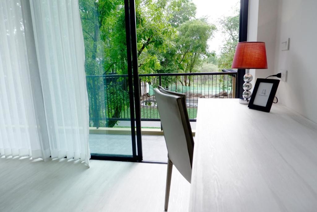 Una habitación con un ventanal grande, una silla, una mesa, una lámpara y un marco de cuadro.
