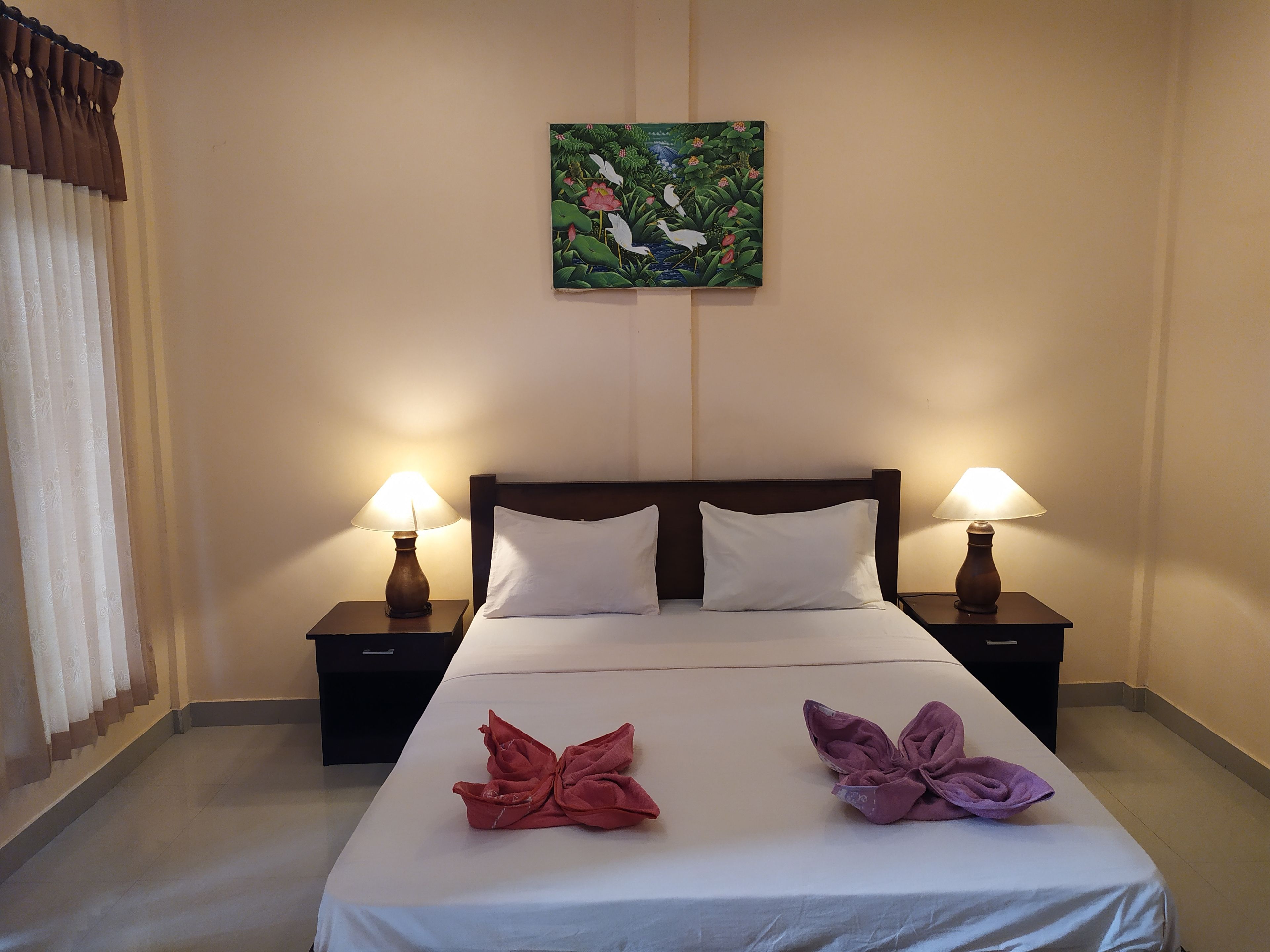 Une chambre d’hôtel avec un lit, deux tables de chevet, deux lampes, un tableau au mur et deux serviettes sur le lit.