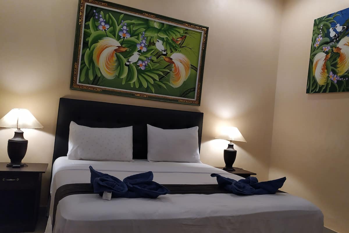 Una habitación de hotel con una cama grande, dos lámparas de noche y dos cuadros con flores en las paredes.