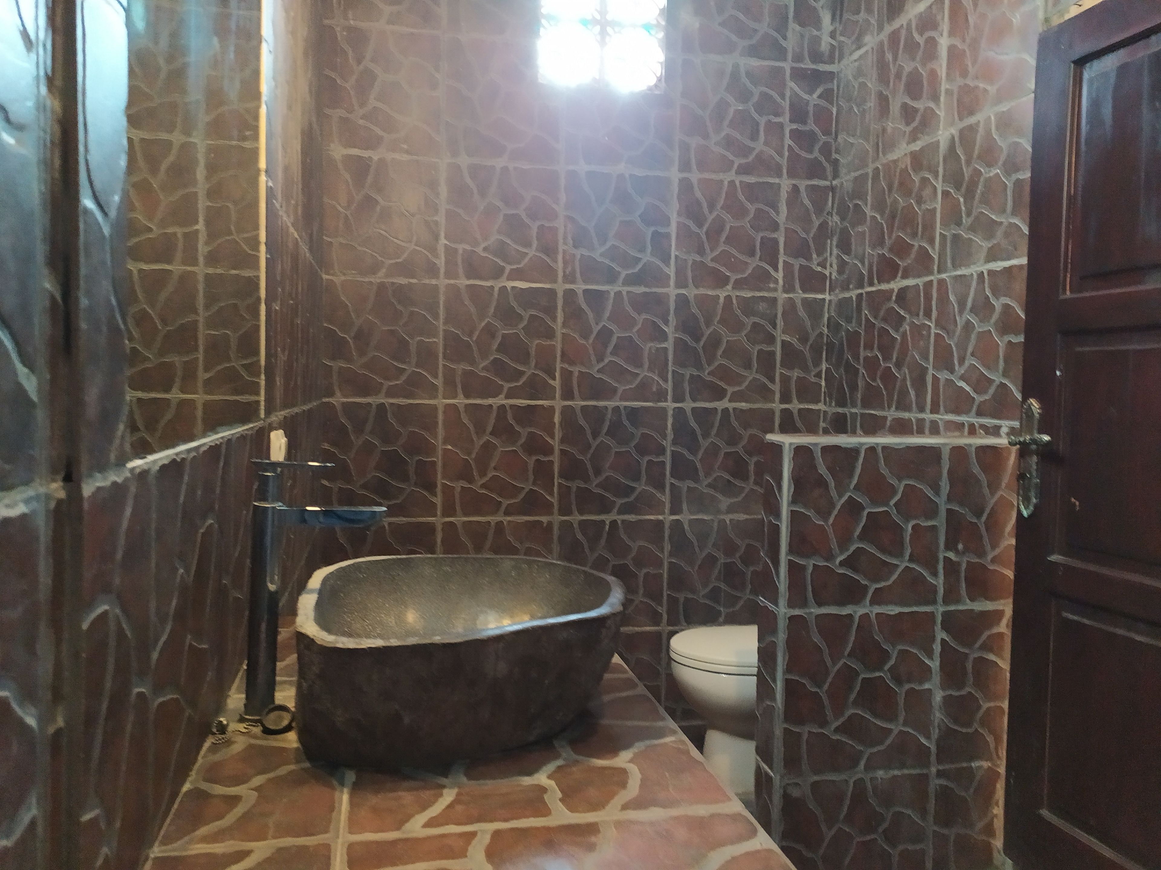 A bathroom with a stone-patterned wall, a freestanding bathtub, and a toilet.
