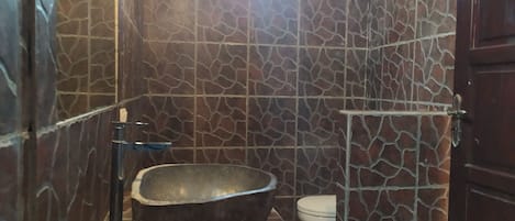 A bathroom with a stone-patterned wall, a freestanding bathtub, and a toilet.
