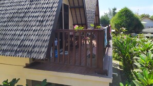 A wooden balcony with a metal mesh railing, surrounded by lush greenery.