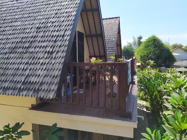 A wooden balcony with a metal mesh railing, surrounded by lush greenery. - Kusuka Bungalows (Gili Trawangan)