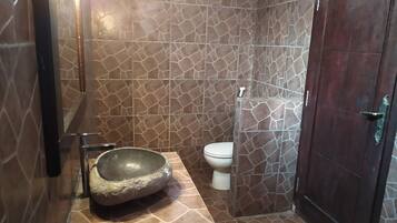 A bathroom with a stone sink, a toilet, and a shower area.