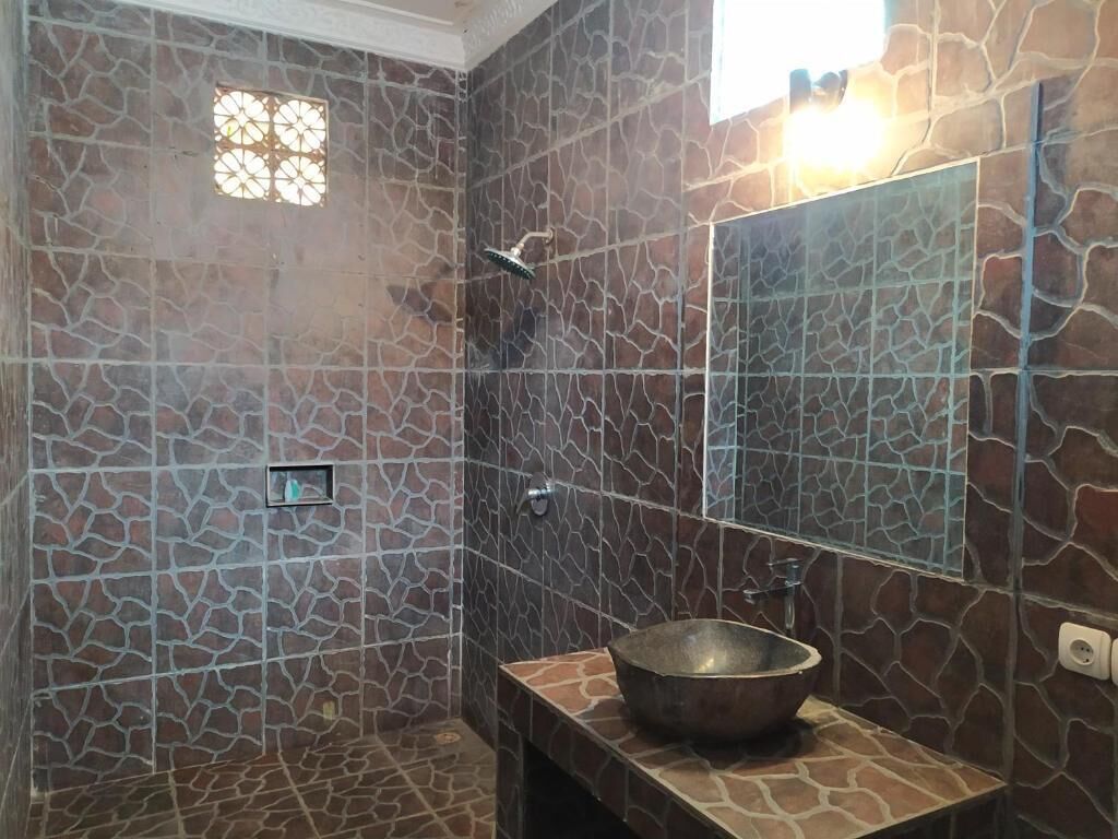Un baño con pared de diseño en piedra, un espejo grande y un lavabo sobre encimera.