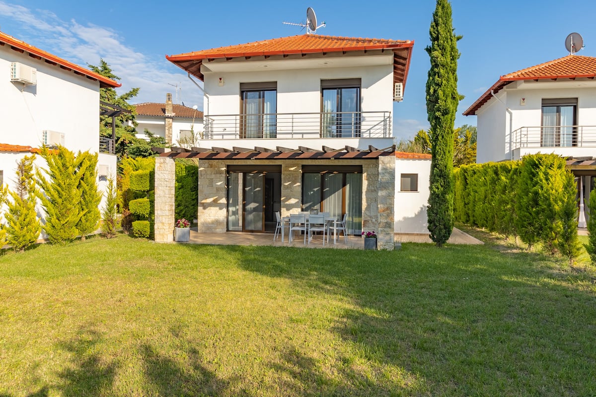 A two-story house with a patio, stone pillars, and a red-tiled roof.