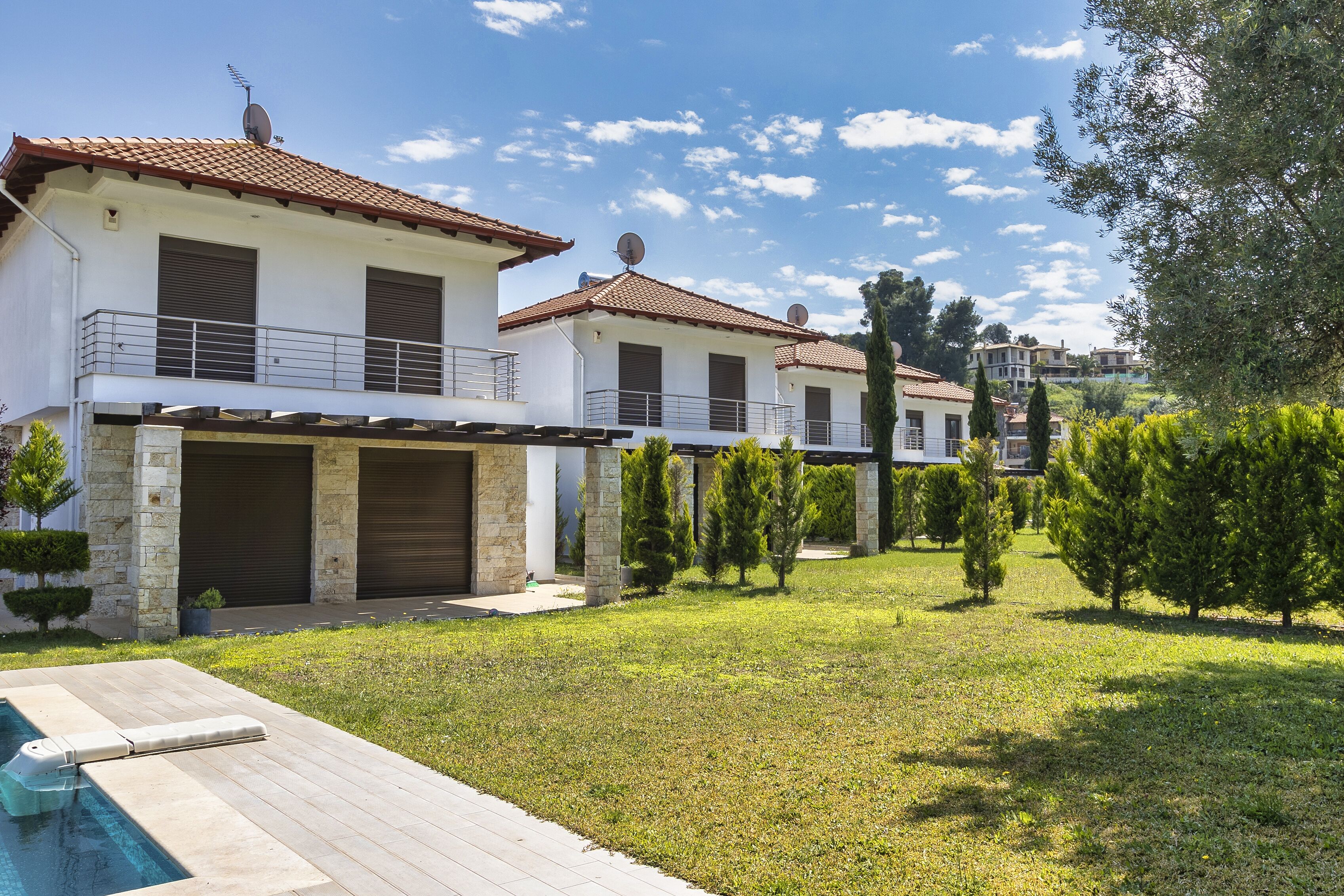 A two-story house with a swimming pool, stone pillars, and a tiled roof.