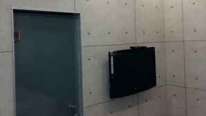 A room with a blue door, a mounted flat-screen TV, and a tiled wall with recessed lighting. - Han Ting B&B (Hualien City)