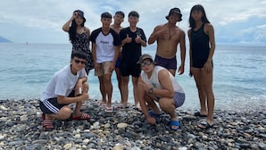 A group of people on a pebbled beach with a clear sky and calm sea in the background. - Han Ting B&B (Hualien City)