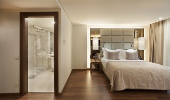 Habitación de hotel con cama, mesita de noche, lámpara y baño con ducha e inodoro.