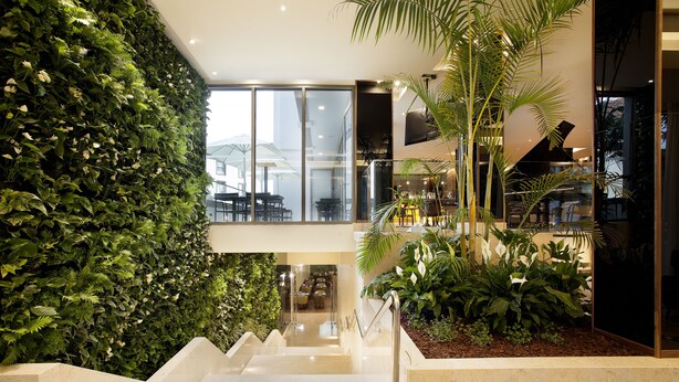 A modern indoor space with a green wall, a staircase, and a seating area with tables and chairs. - Madeira Turim Santa Maria Hotel (Funchal)