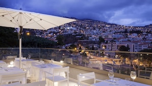 A rooftop dining area with tables set for dinner, overlooking a cityscape at dusk. - Madeira Turim Santa Maria Hotel (Funchal)