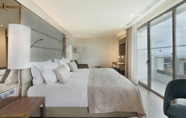 Une chambre d’hôtel moderne dotée d’un grand lit, de tables de chevet, d’un bureau et offrant une vue dégagée grâce à de grandes fenêtres du sol au plafond.
