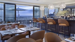 A restaurant with a bar area, large windows with umbrellas, and a view of the cityscape. - Madeira Turim Santa Maria Hotel (Funchal)