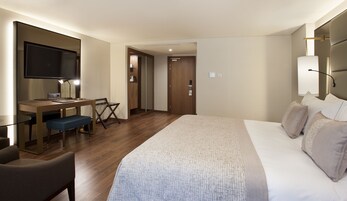 A hotel room with a bed, a desk, a chair, a TV, and a wardrobe.