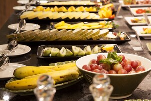 A buffet table with various fruits and vegetables, including bananas, kiwi, and grapes.