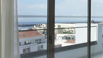 A room with large windows offering a view of the sea and buildings.