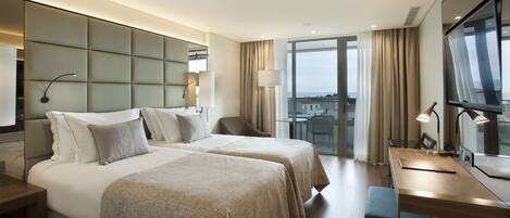 A hotel room with two beds, a desk, a chair, and a large window offering a city view.